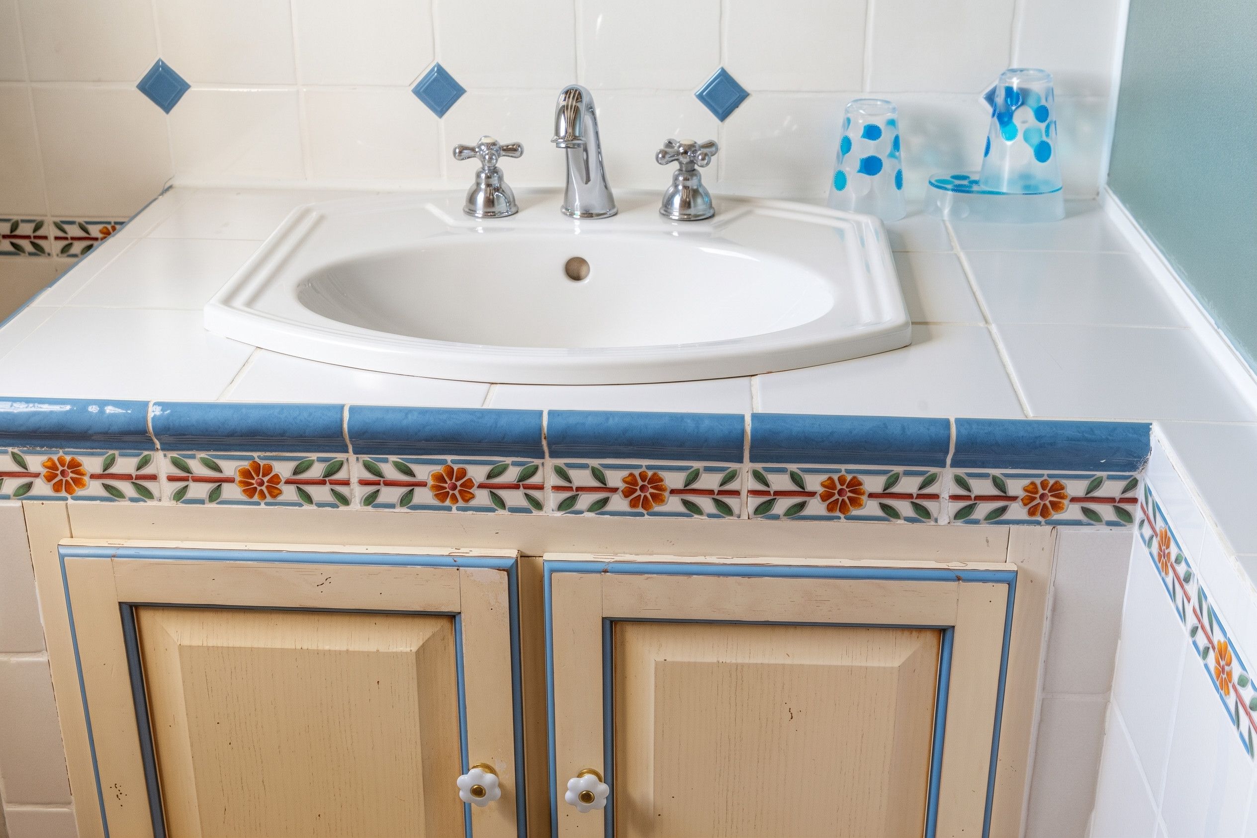 Une salle de bain avec un lavabo blanc, deux robinets et une bordure décorative en carreaux.