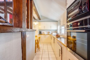 A kitchen with white cabinets, a wooden dining table, and a built-in oven. - Homerez - House in Bangor (Bangor)