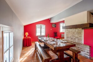 A dining area with a wooden table set for a meal, a red wall, and a stone fireplace. - Homerez - House in Bangor (Bangor)