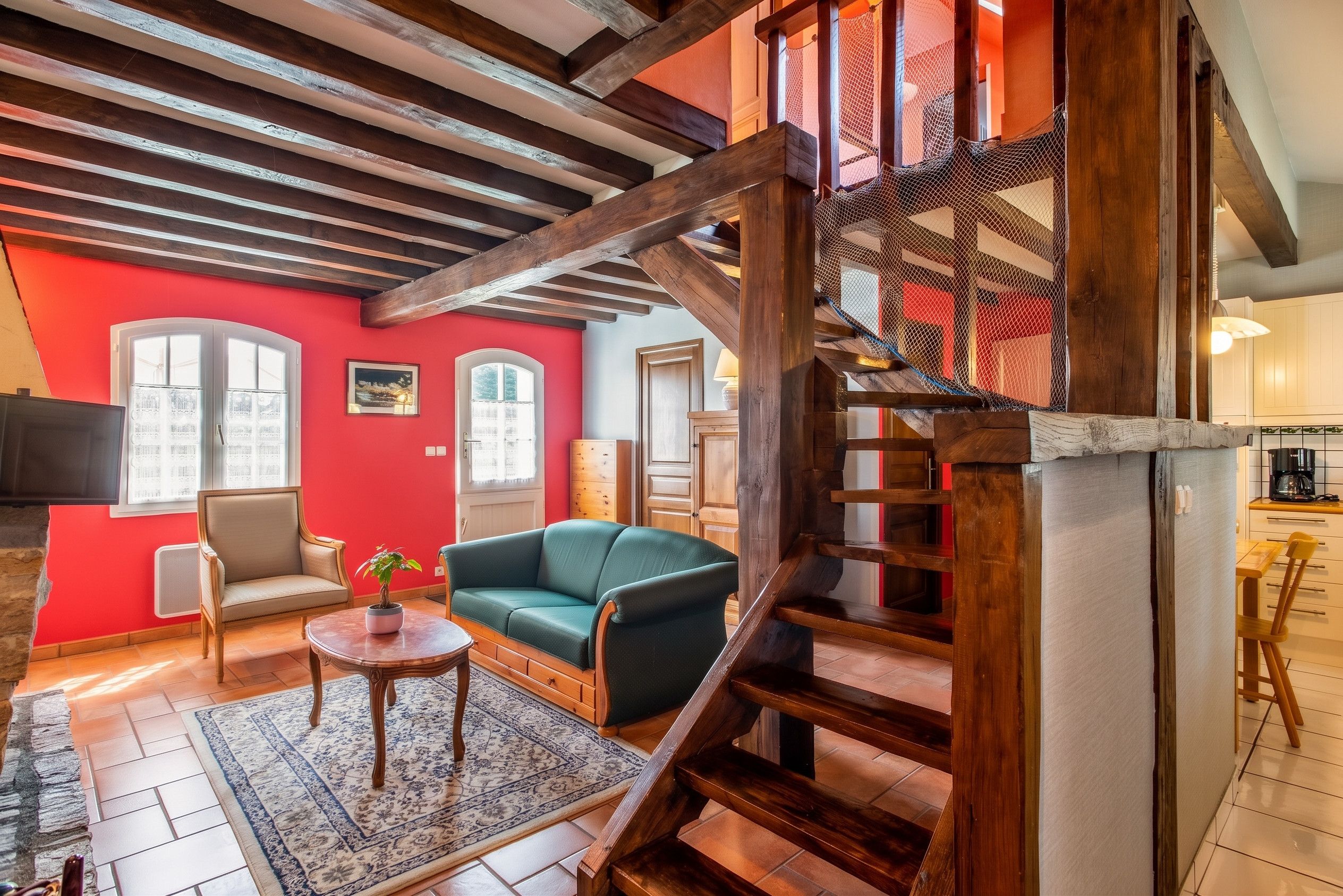 A spacious living area with a green sofa, a wooden staircase, and a red wall.