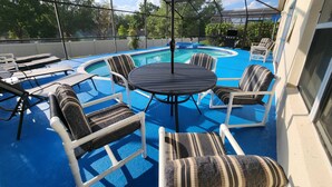 Un área de piscina cubierta al aire libre con una mesa redonda y sillas, rodeada de sillones de descanso con cojines estampados.