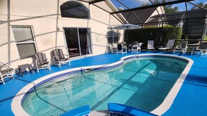 Una piscina interior con bordes de azulejos azules, rodeada de sillones de descanso y un área de patio techada.