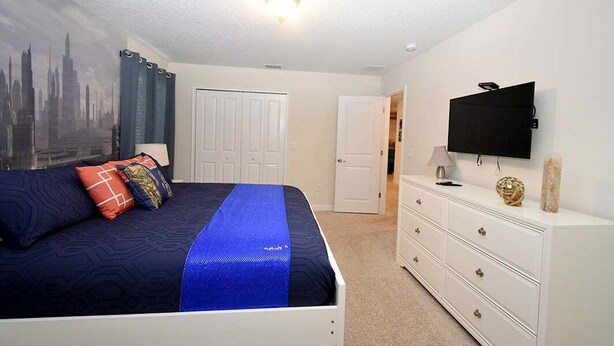 Un dormitorio con cama, cómoda, televisor y puerta que da a otra habitación.