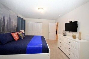 A bedroom with a bed, a dresser, a television, and a door leading to another room.