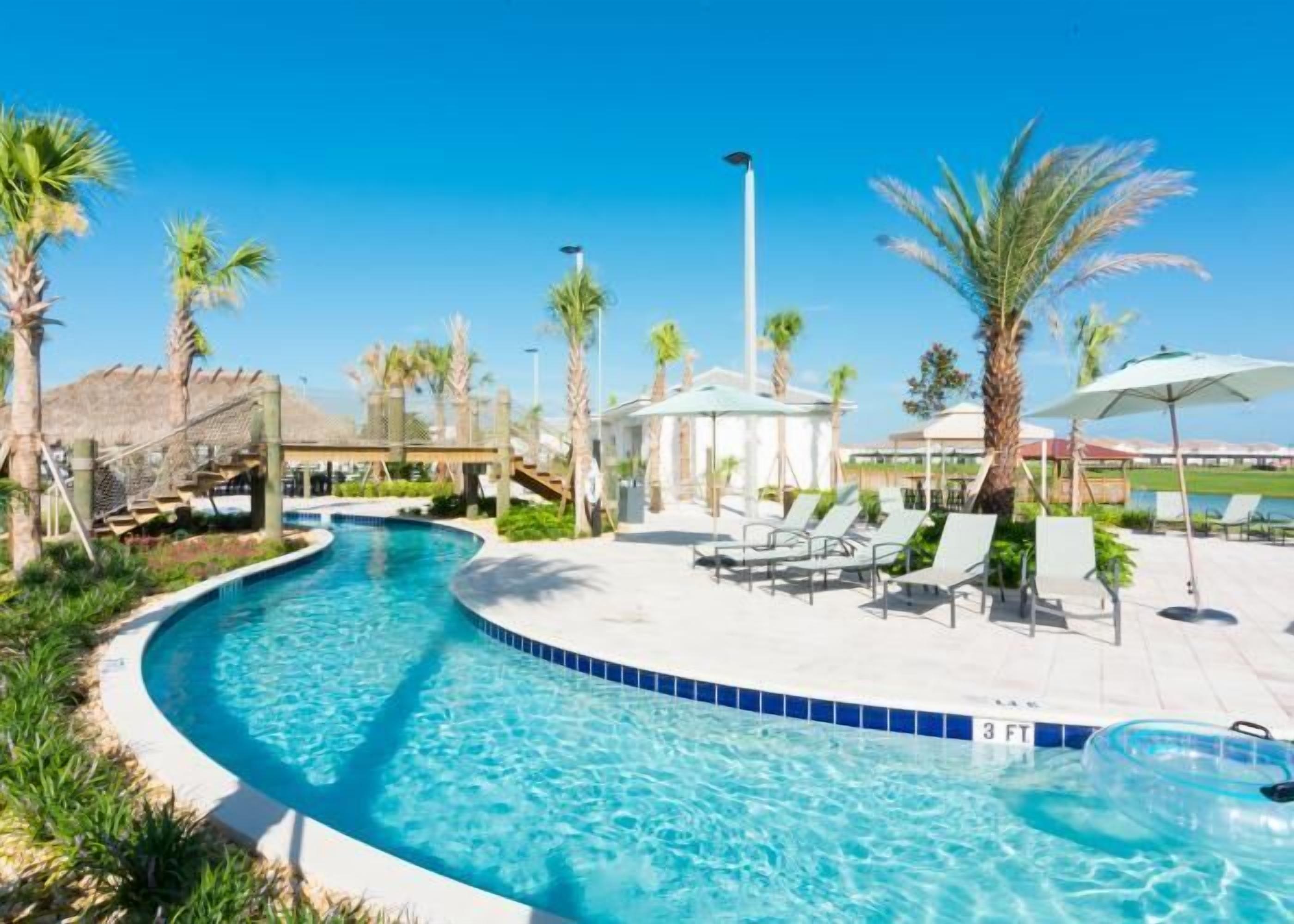 A swimming pool with lounge chairs and umbrellas, surrounded by palm trees.