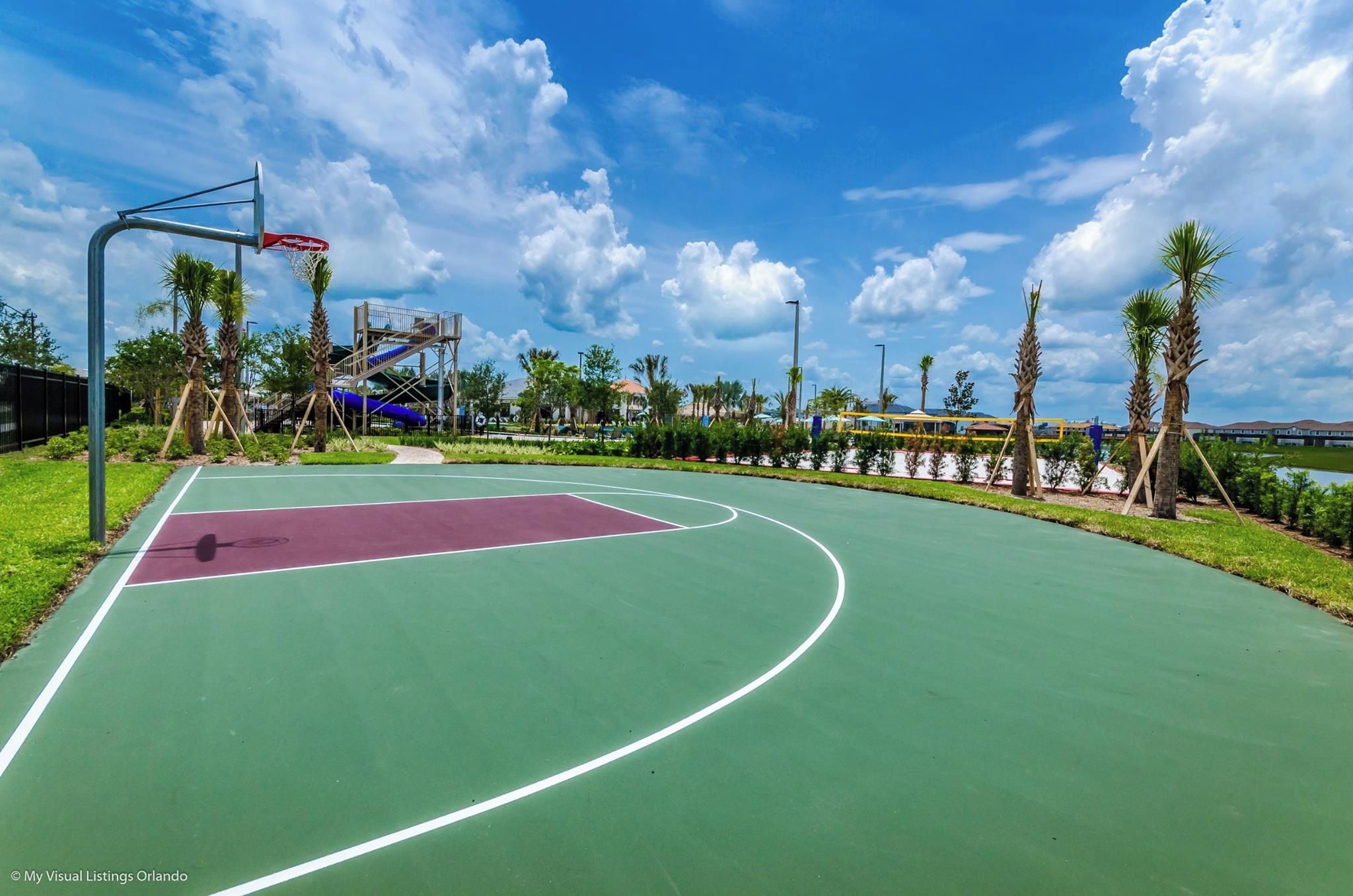 An outdoor basketball court with a clear sky and palm trees.