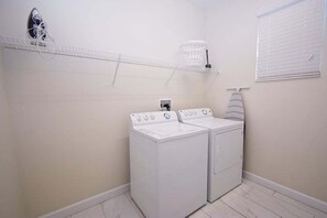 Une buanderie équipée de deux machines à laver blanches, d’un étendoir et d’une fenêtre avec des stores.