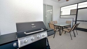 Una cocina al aire libre compacta con una parrilla a gas, una mesa de comedor con sillas y un ventilador de techo.
