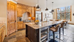 Una cocina amplia con armarios de madera, una isla grande con taburetes de bar, un refrigerador y un ventanal que ofrece luz natural.