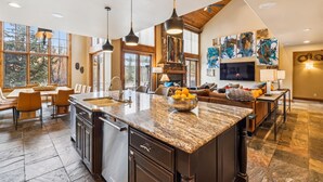 Una cocina amplia con una isla grande, un comedor con mesa y sillas, y una sala de estar con sofá y televisor.