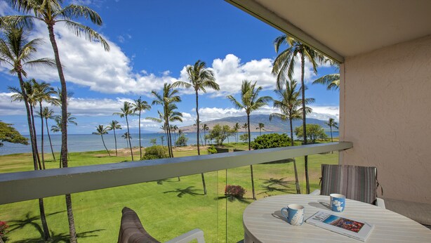 A balcony with a view of a golf course, palm trees, and a body of water.