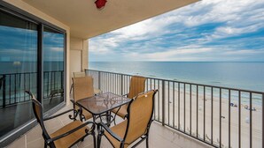 Ein Balkon mit Tisch und Stühlen mit Blick auf einen Strand, bewölkter Himmel und ruhiges Meer.