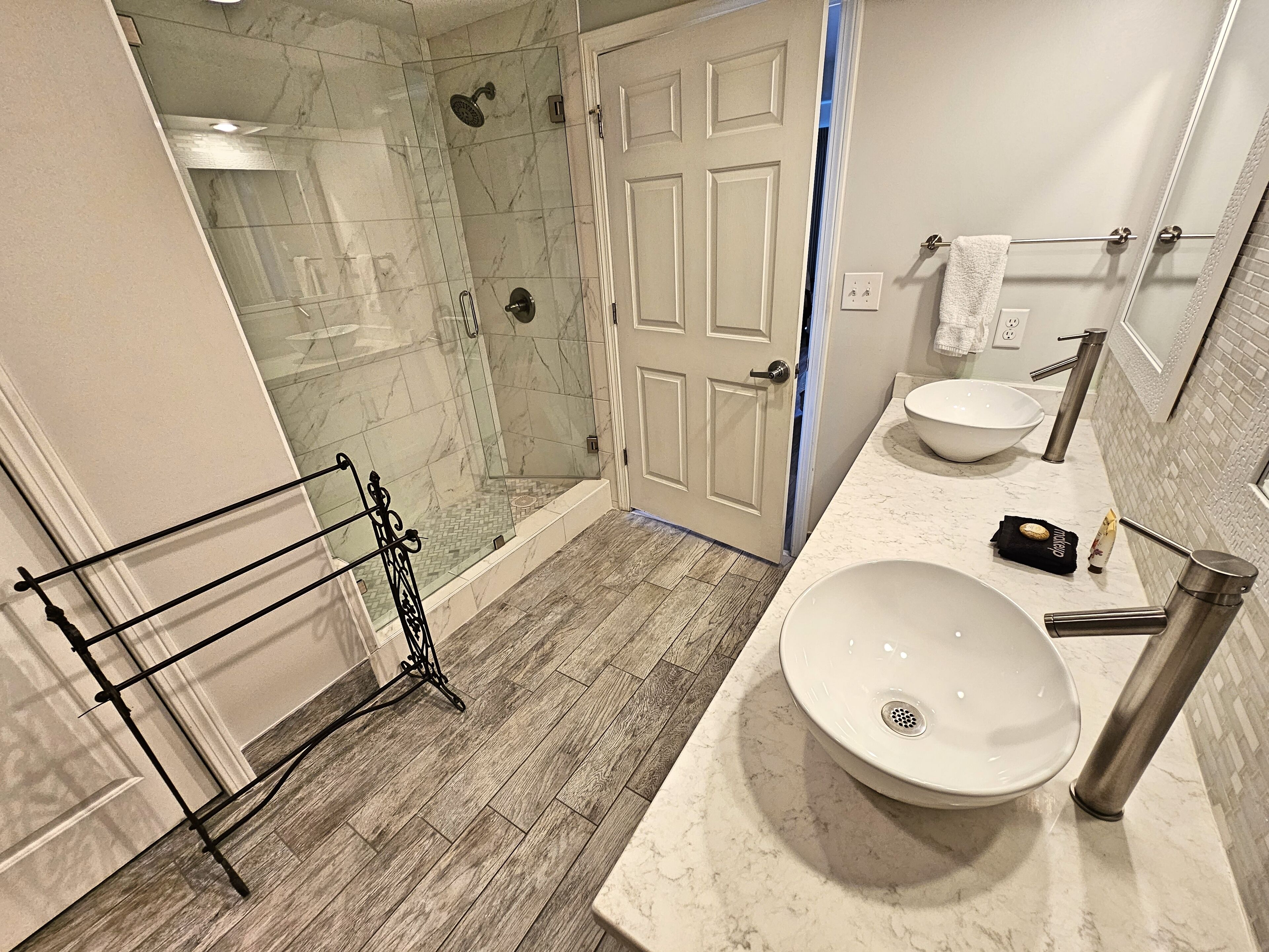 A bathroom with a glass shower enclosure, a white sink with a vessel basin, and a towel rack.