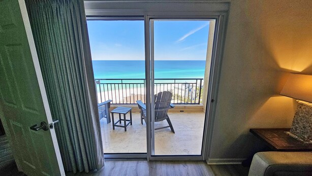Een kamer met een schuifglazen deur die leidt naar een balkon met uitzicht op het strand en de oceaan.