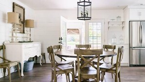 Un coin repas avec une table ronde et des chaises en bois, un buffet blanc et un réfrigérateur en acier inoxydable.