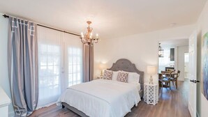 Une chambre à coucher avec un grand lit, un lustre, un coin repas à l’arrière-plan et un tableau au mur.