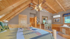 A cozy attic bedroom with a sloped ceiling, wooden beams, a large bed with a colorful quilt, a ceiling fan, a dresser, a mirror, and a window with a view of greenery. - ER258- Sweet Memories Great location- Close to town (Pigeon Forge)