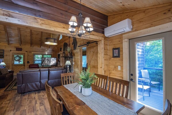 A cozy cabin interior with a wooden dining table, benches, a fireplace, and a large window overlooking the outdoors. - ER258- Sweet Memories Great location- Close to town (Pigeon Forge)