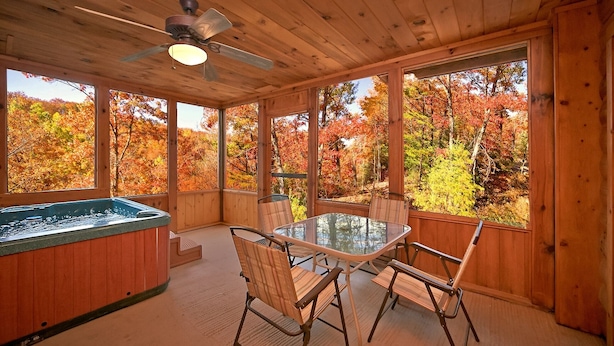 A wooden cabin with a glass table and chairs, a hot tub, and a ceiling fan. - A Secret Hideaway: Pool Table, Convenient, Value (Sevierville)