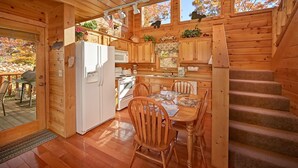 A cabin with a wooden interior, a dining area with a table and chairs, a kitchen with a refrigerator and stove, and a staircase. - A Secret Hideaway: Pool Table, Convenient, Value (Sevierville)
