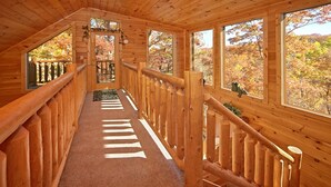 A wooden interior with a central staircase, large windows, and a view of autumn foliage. - A Secret Hideaway: Pool Table, Convenient, Value (Sevierville)