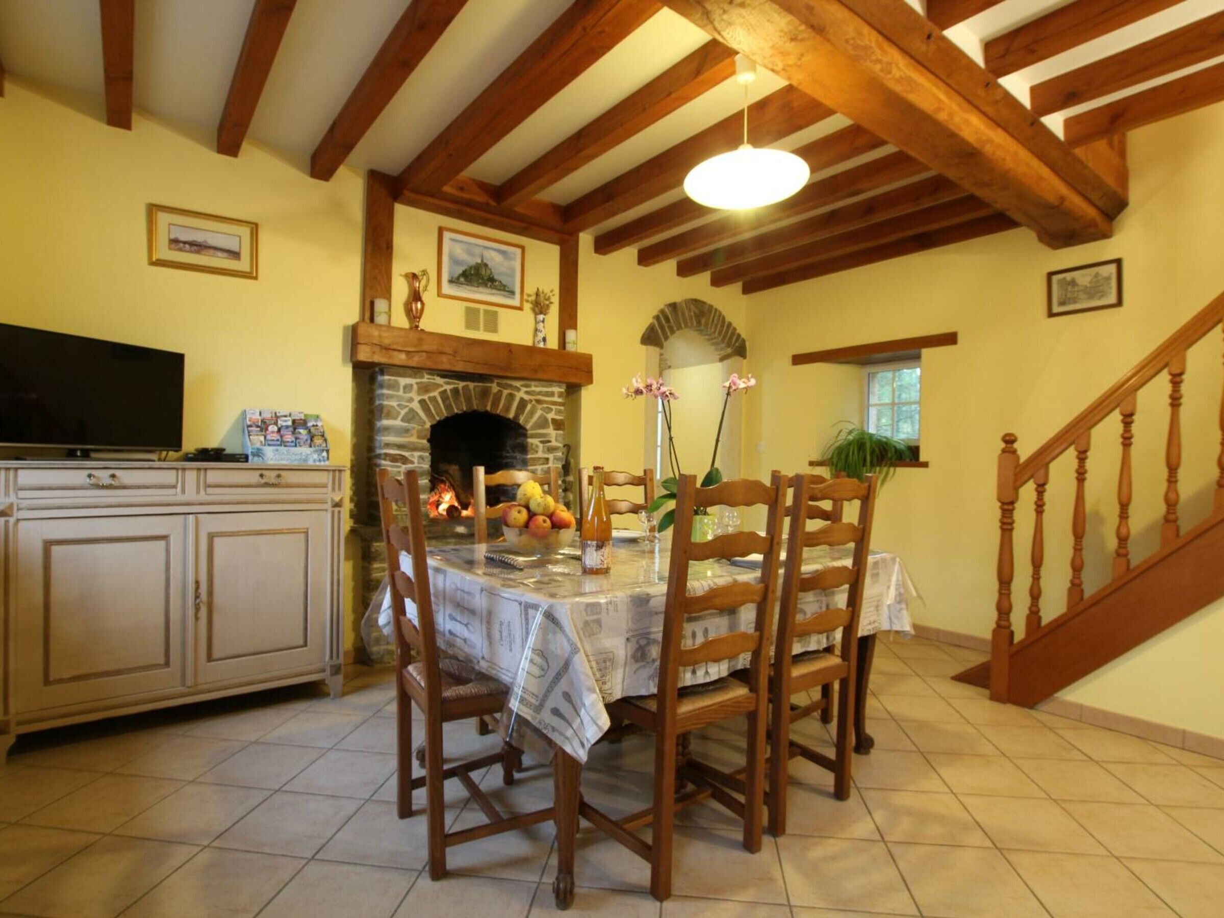 A dining area with a stone fireplace, wooden chairs, a table with a newspaper tablecloth, and a television on a cabinet.