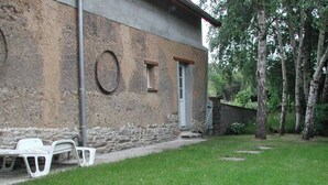 A rustic building with a stone facade, a small window, and a door. There is a white plastic chair and a bench outside. - Bright countryside house with garden and fireplace (Saint-Jean-de-Savigny)