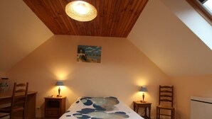 A cozy attic bedroom with a sloped ceiling, a bed with a blue and white patterned bedspread, two bedside lamps, a painting on the wall, and a dining table with chairs. - Bright countryside house with garden and fireplace (Saint-Jean-de-Savigny)