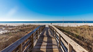 Ein hölzerner Steg führt zu einem Strand bei blauem Himmel.