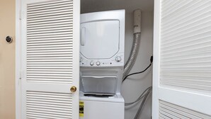 Une buanderie équipée d’un lave-linge et d’un sèche-linge à chargement frontal, d’une porte avec une poignée en laiton et d’un tuyau apparent.