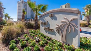 Schild für Royal Palms mit Palmen-Design, umgeben von einem Garten mit verschiedenen Blumen und Palmen.