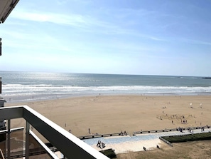 Une vue sur la plage depuis un balcon, avec un ciel dégagé, une plage de sable et l’océan.