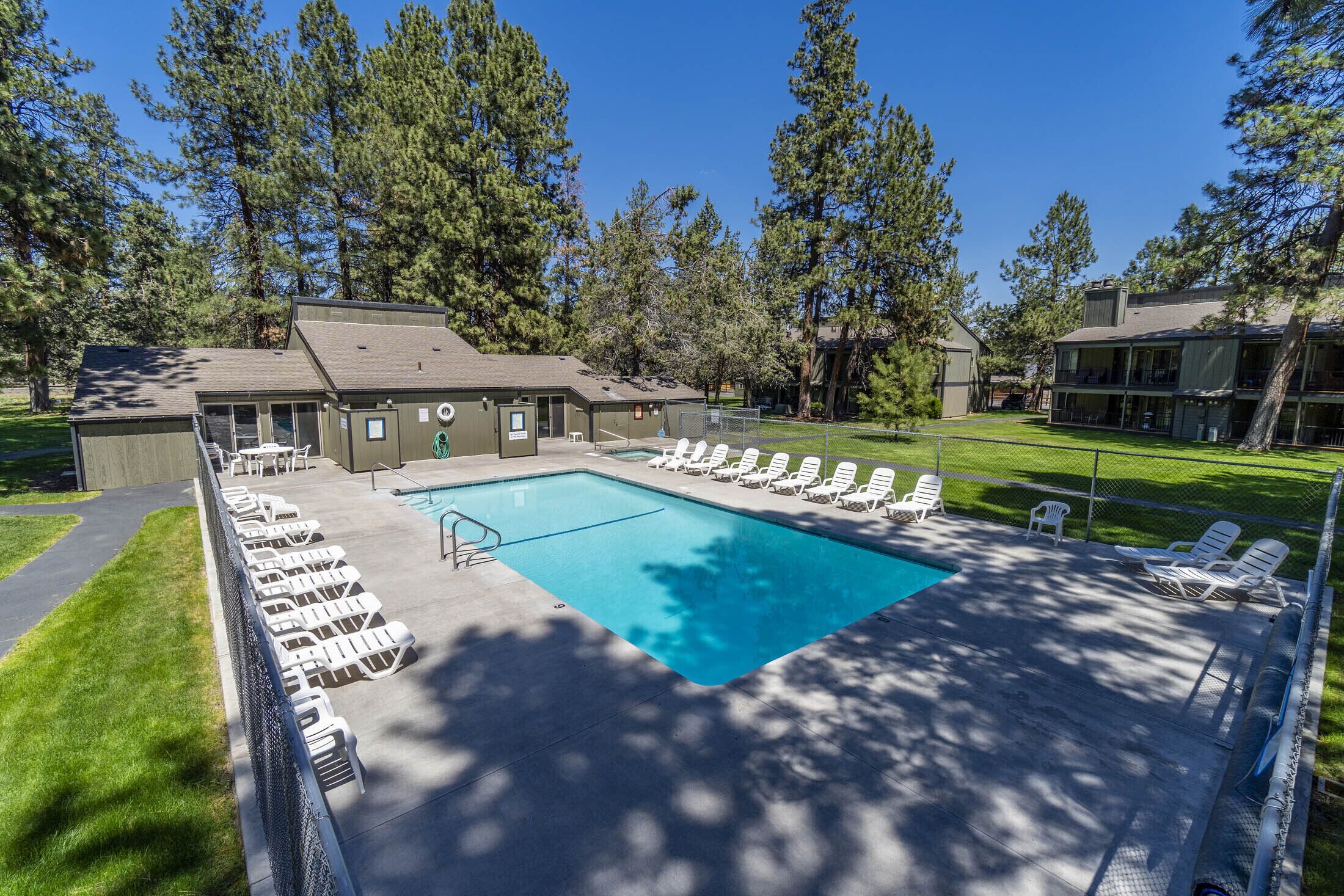 A swimming pool with lounge chairs, a covered patio, and a building with a fenced yard.