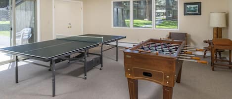 Um quarto com mesa de pingue-pongue, mesa de futebol de mesa e uma porta que dá para um pátio com área de estar ao ar livre.