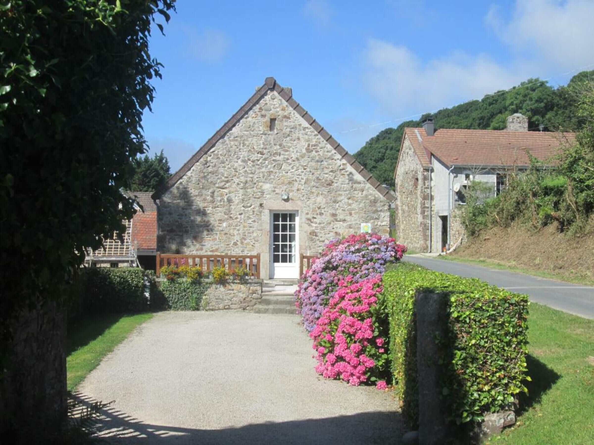 A stone building with a gabled roof, a gravel driveway, and a flower bed with pink and purple flowers.
