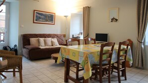 A cozy living room with a brown sofa, a dining table with chairs, a TV, and a framed picture on the wall. - Holiday home 4 pers, private garden, in La Hague (Vasteville)