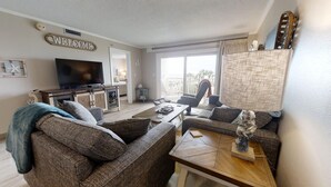 A living room with a television, sofas, a coffee table, and a balcony with a view. - 🌅 Islander #301 – Luxury Beach Living, Steps to the Sand! 🌊🐬 (Destin)