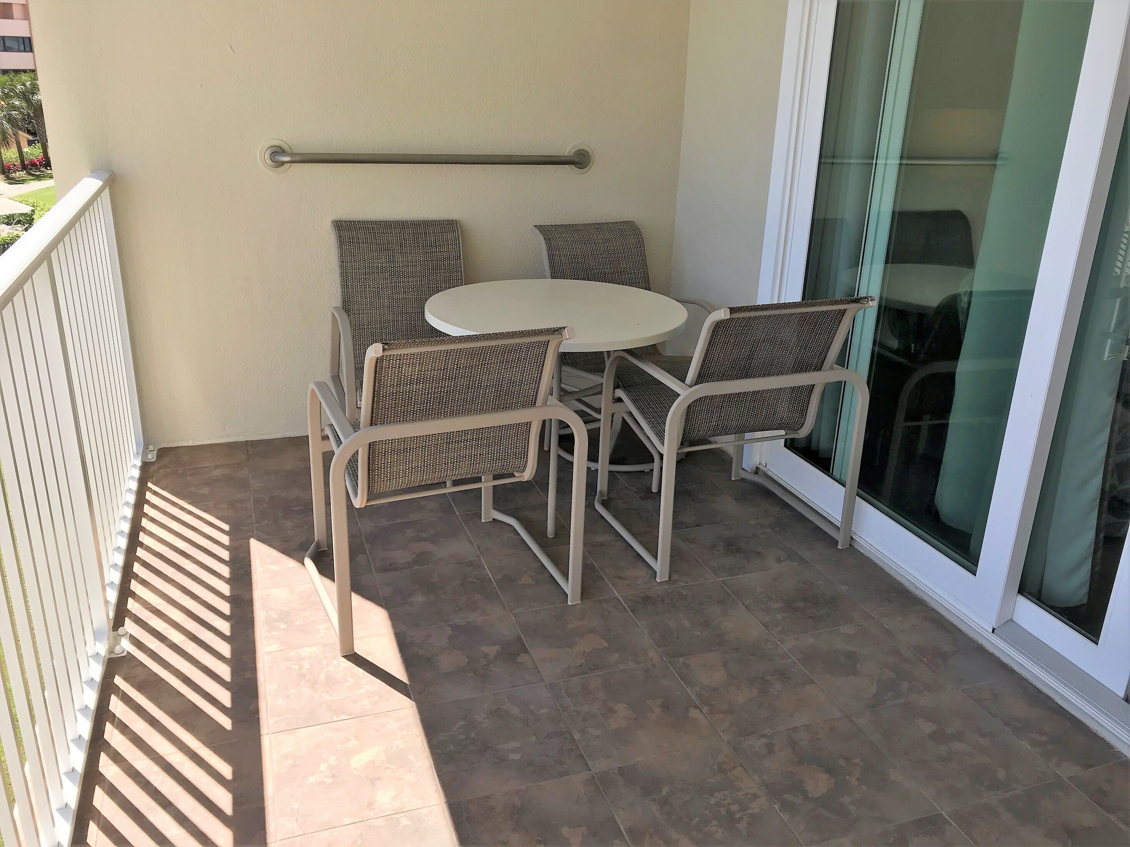 A balcony with a round table and four wicker chairs, a metal railing, and a sliding glass door.