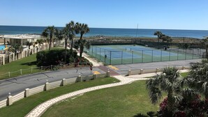 A tennis court with a view of the ocean, surrounded by palm trees and a fenced area. - 🌅 Islander #301 – Luxury Beach Living, Steps to the Sand! 🌊🐬 (Destin)