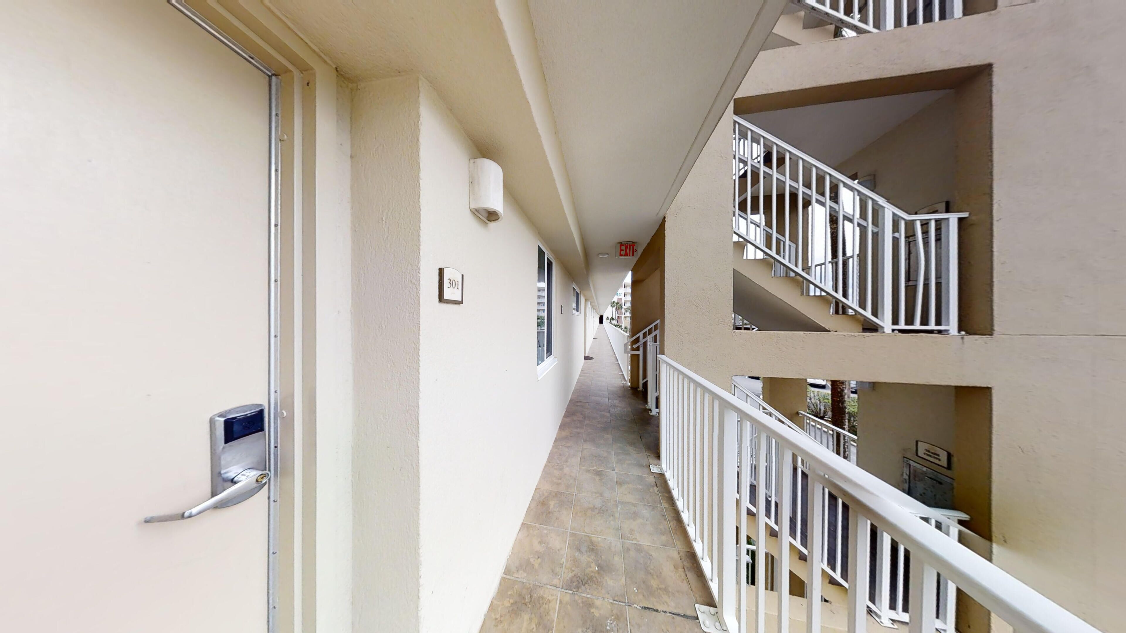 A corridor with a door on the left, a sign indicating room 301, and a staircase leading to an upper floor with balconies.