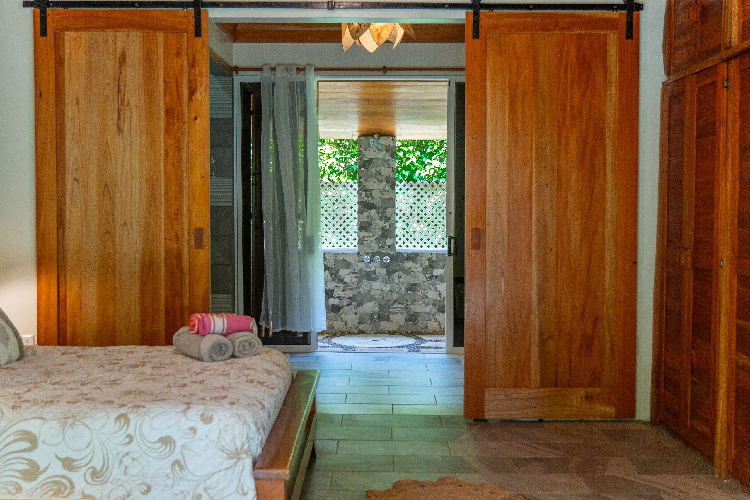 Un dormitorio con cama, una puerta de madera y vistas a un espacio exterior con muro de piedra y vegetación.