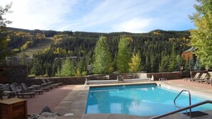 A pool area with a hot tub, lounge chairs, and a view of a forested hillside.