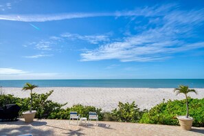 A beach view with a clear sky, a sandy beach, and two lounge chairs.