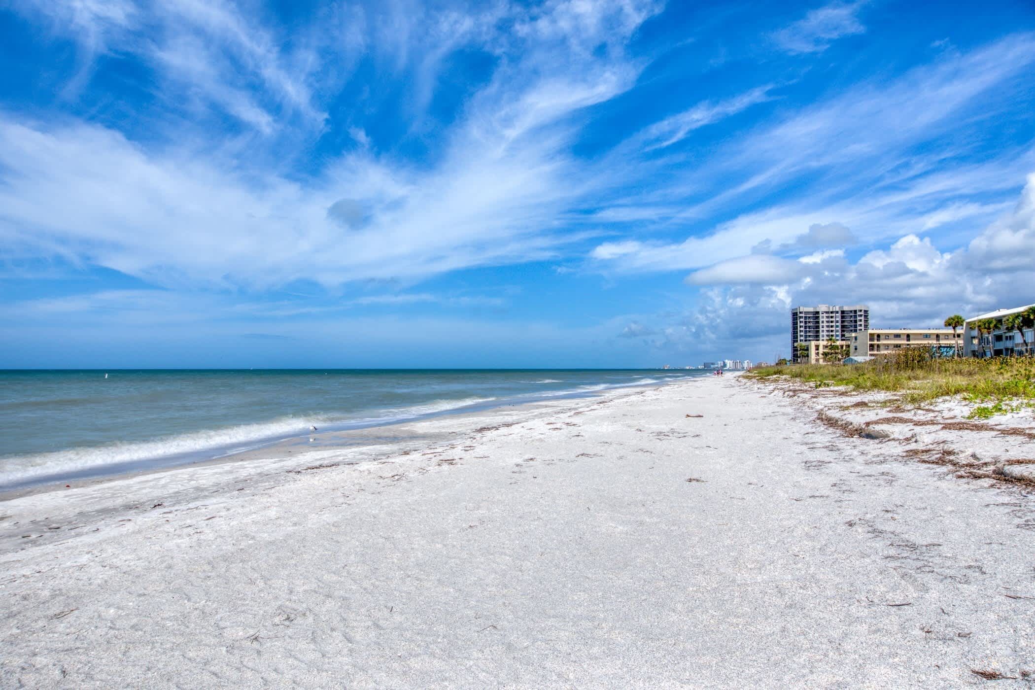 A beach with a clear sky and ocean. There are buildings on the right side of the beach.