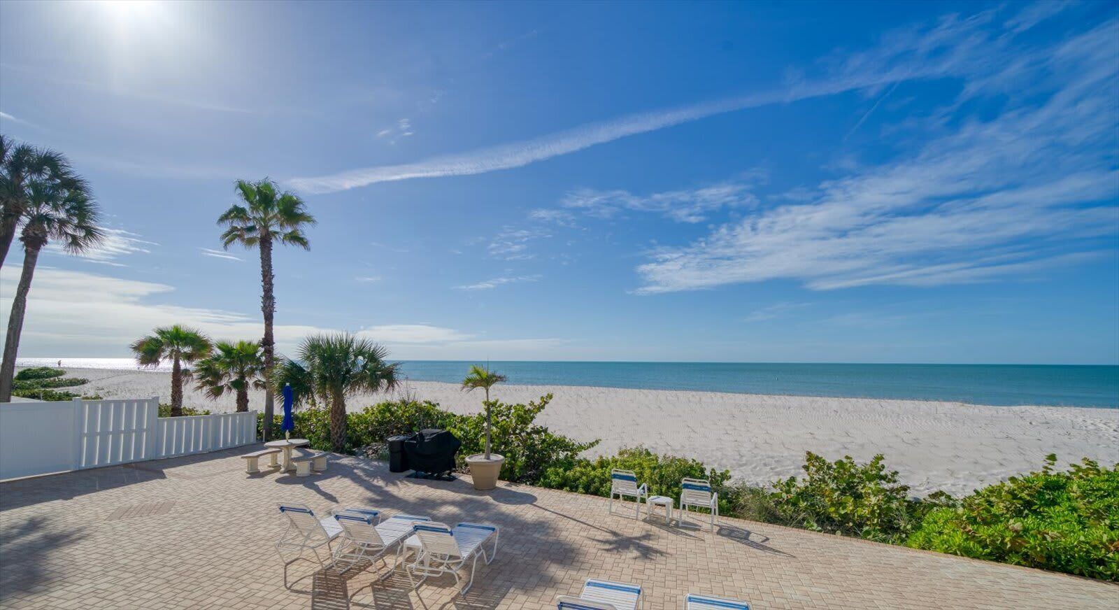 Een terras aan het strand met loungestoelen, een barbecue en uitzicht op de oceaan.