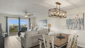 Ein modernes Wohnzimmer mit Sofa, Esstisch und Stühlen. Es gibt einen Deckenventilator, eine Kronleuchter und Kunstwerke an den Wänden.