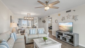 Ein modernes Wohnzimmer mit Deckenventilator, Fernseher, Sofa, Couchtisch und einem Essbereich im Hintergrund.
