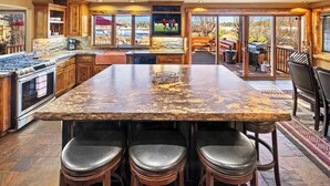 A spacious kitchen with a large island, bar stools, and a view of the outdoors. - Cienega Lakeview by Destination Big Bear : Spectacular Luxury Lakefront! HOT TUB W/Lake and Mountain Views! Game Room with Pool Table! Gourmet Kitchen! (Big Bear Lake)