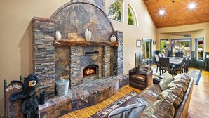 A cozy living room with a stone fireplace, leather sofa, and a bear decoration. - Cienega Lakeview by Destination Big Bear : Spectacular Luxury Lakefront! HOT TUB W/Lake and Mountain Views! Game Room with Pool Table! Gourmet Kitchen! (Big Bear Lake)