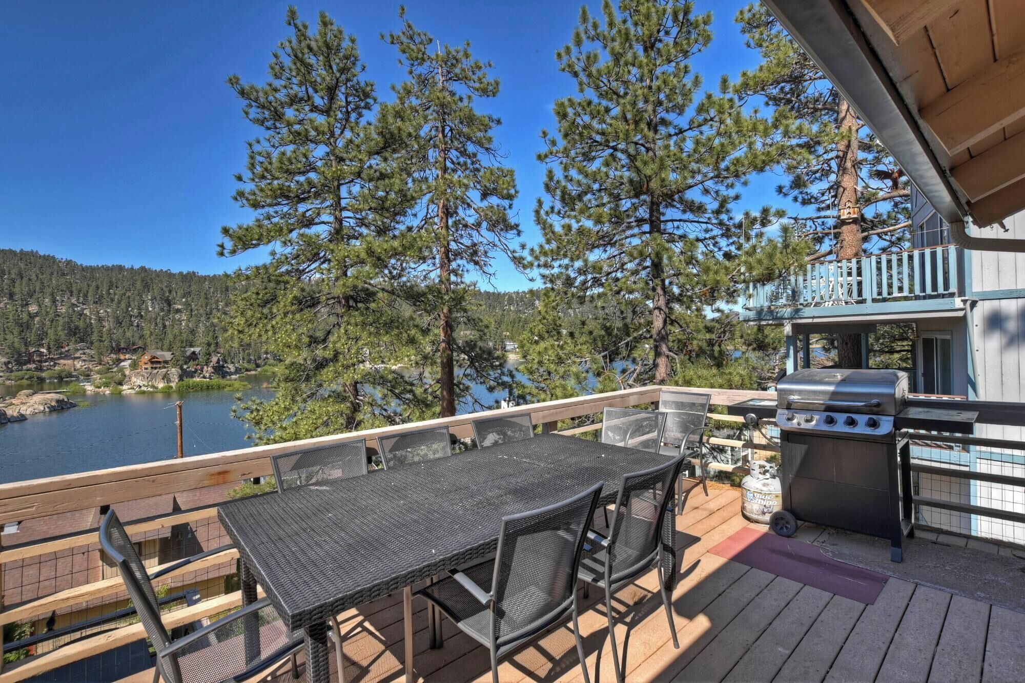 A deck with a table and chairs, overlooking a lake and forest.